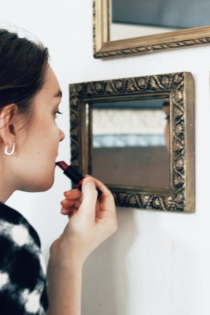 Crop unrecognizable woman using lipstick in front of mirror indoors